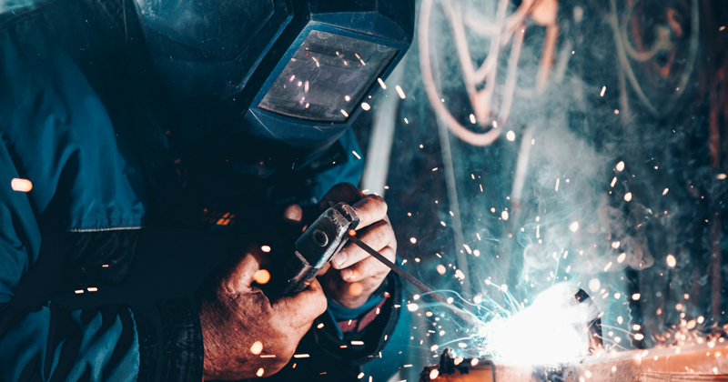 Facilities services person wearing a mask and welding with sparks flying toward the camera